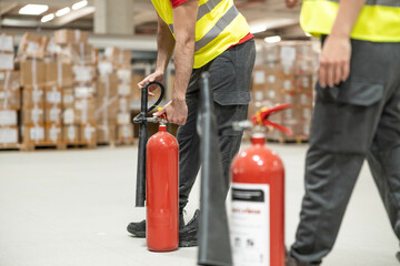 Close-up of male warehouse worker training with fire extinguisher during safety drill.