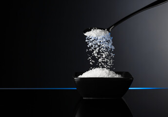 Sea salt in a small ceramic bowl on a black reflective background.