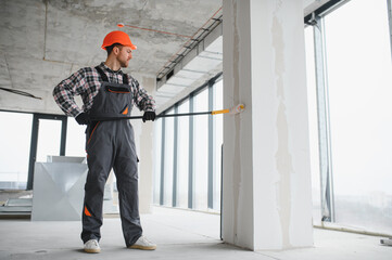 Construction worker painting wall with roller in building under construction