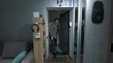 A man opens the door and enters the room. A stylish man in a hat enters the apartment. A young man in the house opens the door. Slow motion.