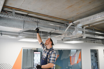 Construction worker installing ventilation system in modern office building
