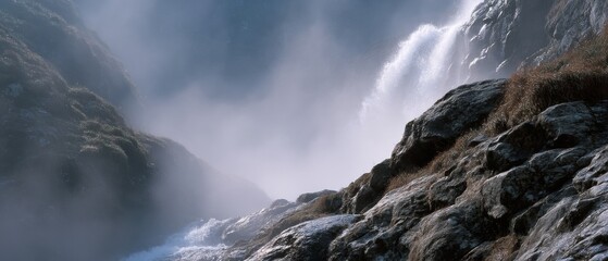 Misty waterfall cascades down rocky cliffs, creating a mystical and serene atmosphere in a tranquil natural landscape.