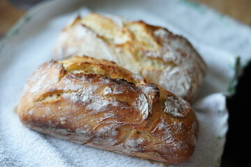 Rustic homemade crusty bread on a white cloth with a slice topped with a piece of butter.