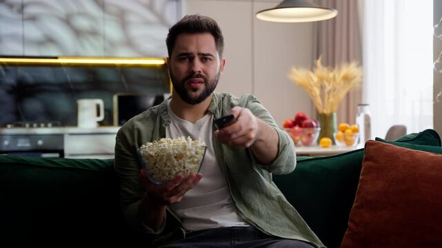 Upset unhappy sad Caucasian man male homeowner guy spectator holding bowl popcorn snack broken controller boring show error resting failed relaxing failure bad channel sitting sofa at home living room