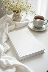 Mockup of a book on a table, a mug of hot delicious tea and a vase with beautiful flowers. Sunny weather. For your creative designs.