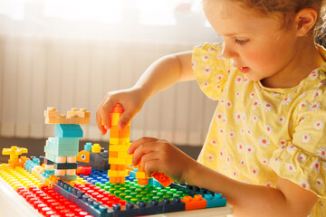 Child's hands busy building with vibrant toy constructor blocks on a baseplate, demonstrating...