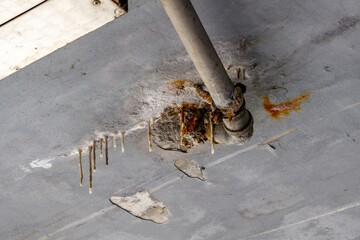 Close-up of a damaged section on a flat roof with cracked insulation around a pipe, visible signs of rust, leaks, and surface cracks. Corroded elements and stains indicate water infiltration and poor 