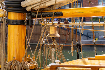 Fototapeta premium close-up of a traditional sailing ship, featuring a wooden mast, rigging, a ship's bell, and deck elements. The warm-toned wood and numerous ropes create a nautical atmosphere, highlighting the crafts