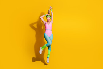 Cheerful young woman jumping in colorful retro activewear on vibrant yellow background