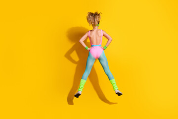Plakat Energetic young woman in colorful retro workout attire jumping in front of a vibrant yellow background, embodying fitness