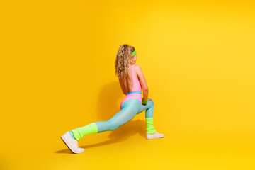 Energetic young woman in vibrant sportswear doing workout exercises against a yellow background