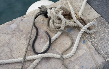 Intricately tangled ropes resting on weathered stone dock beside tranquil water surface creating...