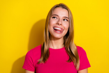 Cheerful young woman in a bright pink t-shirt making a playful expression against a vibrant yellow...