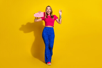 Young stylish woman posing with a skateboard against a vibrant yellow background, showcasing colorful fashion and a playful smile