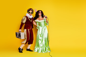 Young couple in elegant medieval costumes enjoying a lively masquerade party with a vibrant yellow background