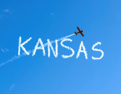 Airplane skywriting 'kansas' in clear blue sky with smoke trails