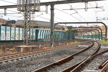Urban railway station with graffiti-covered train cars and tracks in a bustling city environment