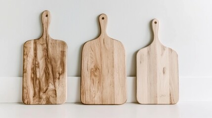 Three wooden cutting boards of different sizes and shapes, arranged in a row against a white wall.