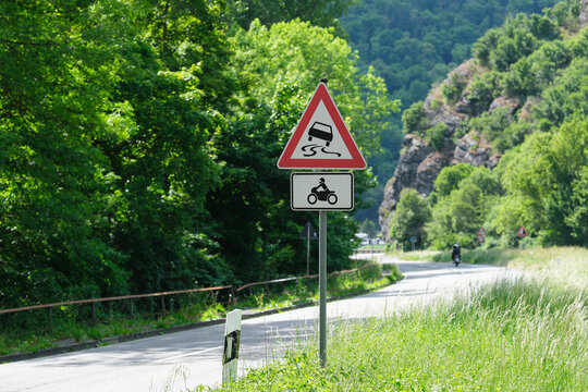 Kurvenreiche Stra&szlig;e und Verkehrsschild mit Verkehrszeichen Schleudergefahr und Rutschgefahr und Zusatzschild Kraftr&auml;der, Kleinkraftr&auml;der und Mofas - Stockfoto