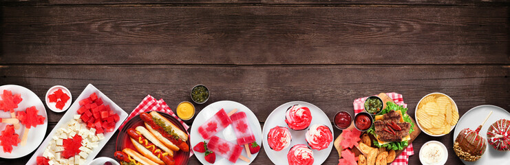 Canada Day patriotic food. Top down view bottom border on a dark wood banner background. Hot dogs, hamburgers and maple leaf red and white theme snacks. Copy space.