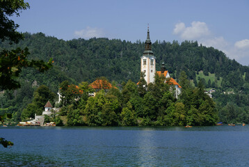 Obraz premium very small island on natural bled lake in summer with church in middle and beautiful green trees around with blue waters and clear blue sky