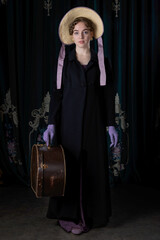 A Regency woman wearing a travelling attire and a bonnet, and standing with a leather hat box