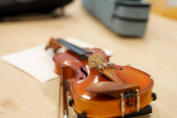 Violin resting on a table with music sheets and instrument case nearby in a light-filled room...
