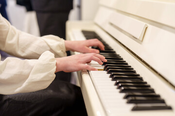 Fototapeta premium Hands playing elegant melodies on a white piano in a softly lit room during a musical evening event