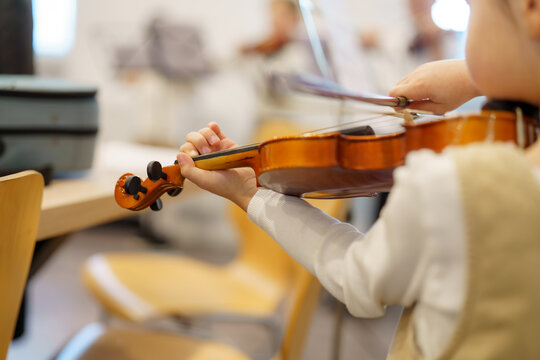 Child practicing violin during a music class in a bright classroom environment with wooden chairs