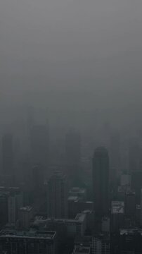 Aerial video shot of a cityscape shrouded in dense fog, creating a mysterious and moody atmosphere with skyscrapers barely visible. Live mobile wallpaper.