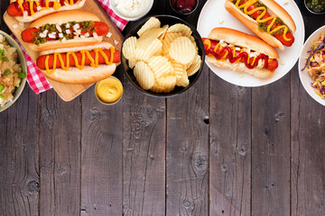 BBQ top border with hot dogs, classic salads and snacks. Above view table scene over a dark wood background. Copy space.