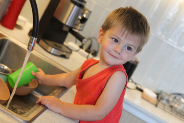 portrait of cute toddler boy washing dishes  in the kitchen sink