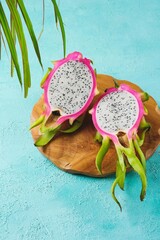 Fresh pink skinned pitahaya or dragon fruit cut in half on wooden board against turquoise concrete...