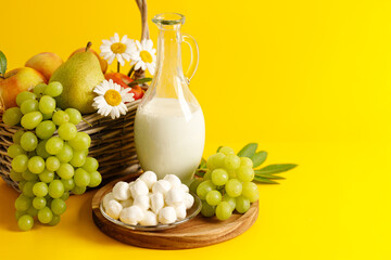 Wicker basket with fruits, wheat ears and dairy products on yellow background, Shavuot concept