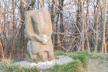 Outdoor image of an ancient, weathered stone sculpture depicting a seated human figure Rustic and...