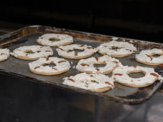 A baking sheet holds ring-shaped breads topped with cream cheese frosting and scattered pecan pieces