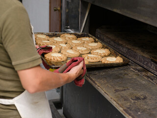 A baker's hands remove a tray of golden-brown pastries from a commercial oven