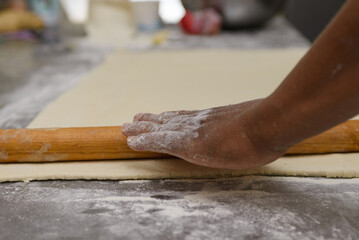 A hand guiding a wooden rolling pin across a sheet of dough, dusted with flour on a counter top