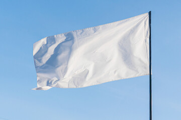 Close-up of a large, frayed white flag against pale blue sky and beige background, hung from a...