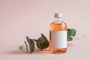 A minimalist product photography shot of a clear glass bottle containing rose-colored liquid against a soft pink background