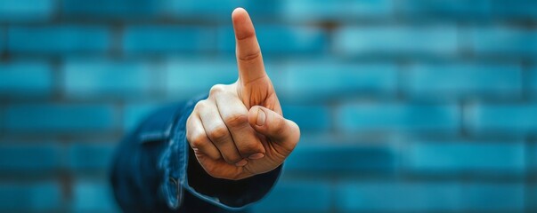 A hand pointing upward with a finger extended against a blurred blue brick wall background image