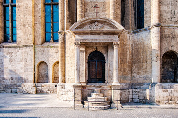 Travertine stone embellishing the Cathedral of Saint Emidius facade in Ascoli Piceno reveals an ancient side entrance with a gated archway, steps, and a cross