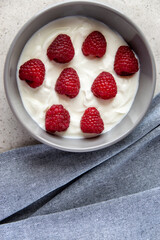 Gray bowl and natural yogurt with red raspberry on the stone marble table.