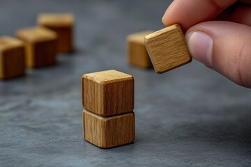 Hand stacking wooden blocks on a gray surface.