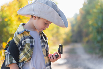 Boy with explorer hat looking at compass on forest trail © Irina