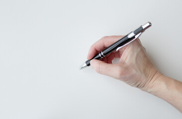 Caucasian hand holding a black business pen to write a message or sign a document. Writing, office supplies. Copy space available on white background.