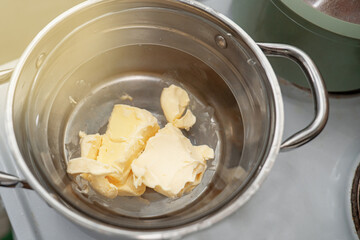 Pieces of butter melting in a glass bowl over a steam bath in a metal pot, perfect for baking or cooking preparations