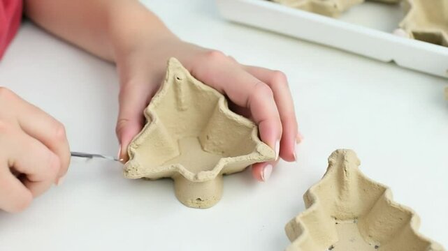 Hands make festive Christmas crafts with recycled egg carton clay. Follow step-by-step instructions to create unique Christmas tree shaped decoration for your holiday celebrations.