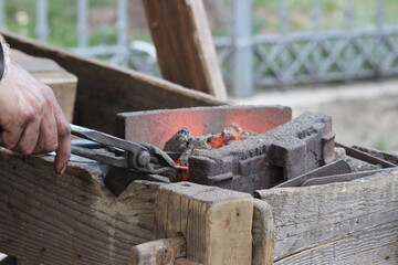 A blacksmith heats a piece of work on coals, holding it with tongs