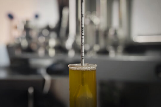 Hydrometer floating in a yellow liquid inside a graduated cylinder, used for measuring specific gravity in a laboratory setting - Powered by Adobe